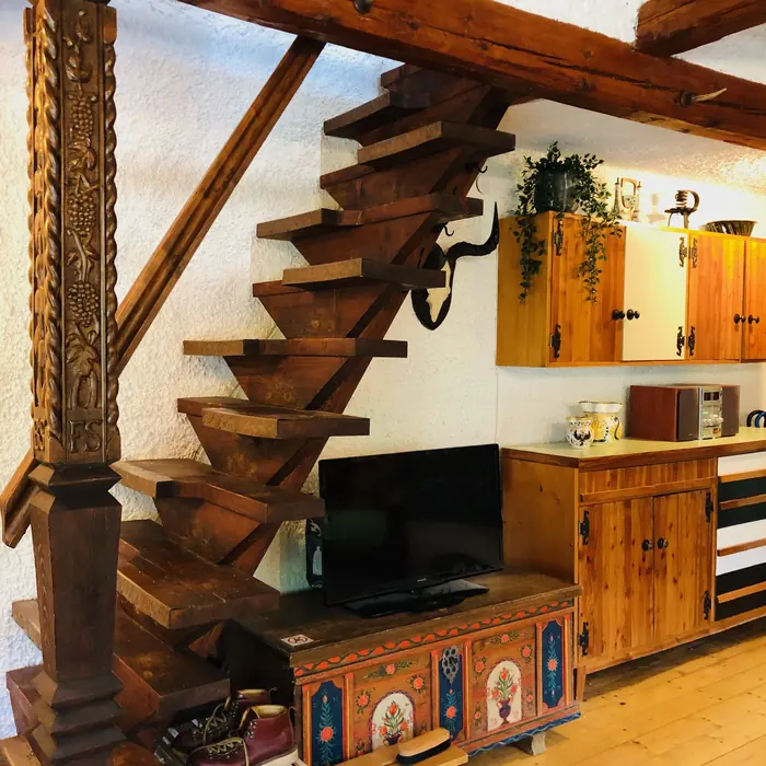 Wooden staircase past a traditional hand-painted chest and the living-room TV nook