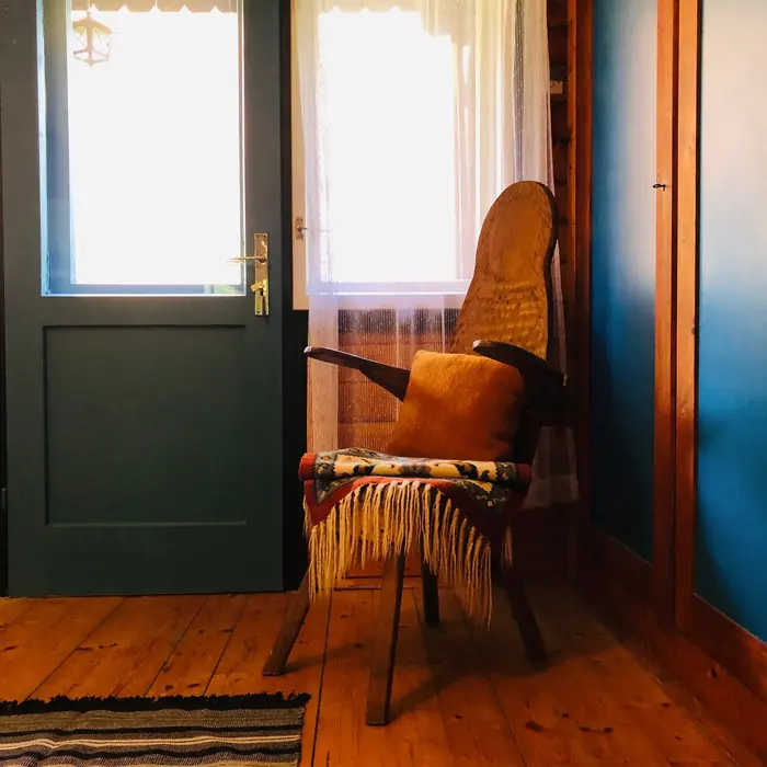 A rustic upholstered chair with a woven throw, beside a lace-curtained window